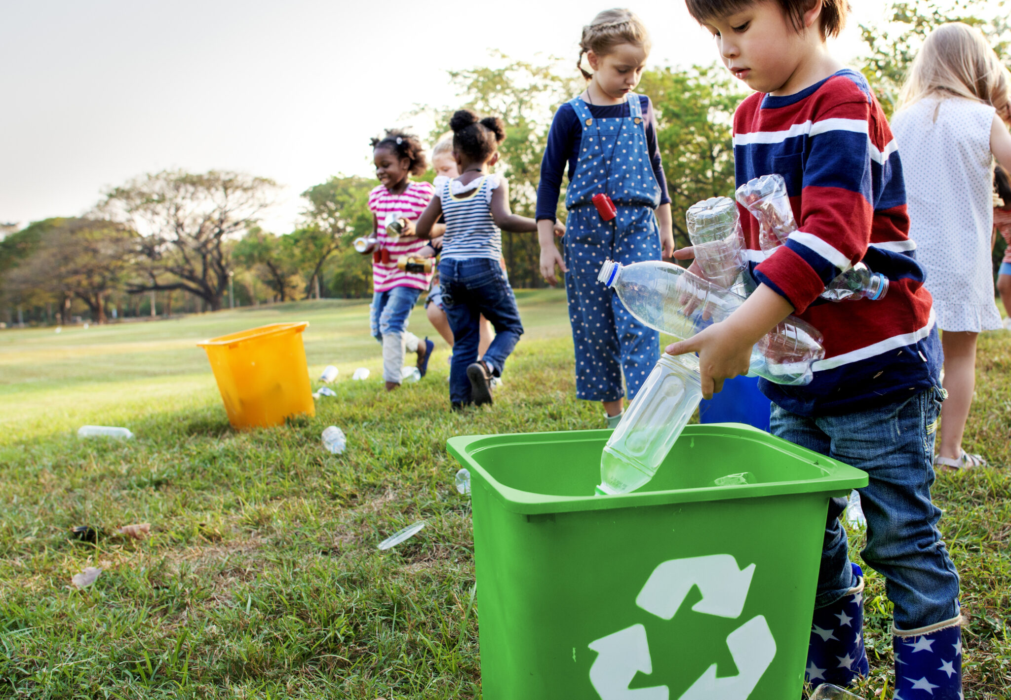Children recycling plastic bottles outdoors in a park.