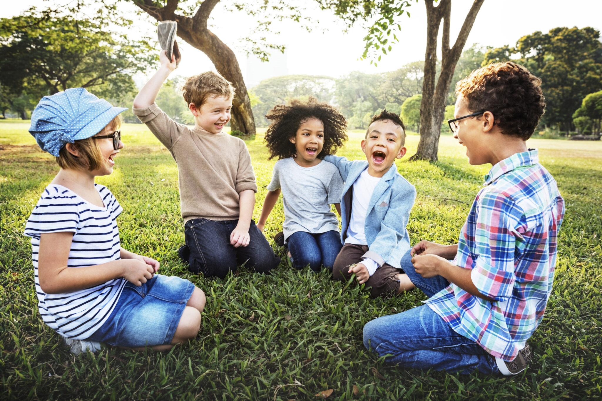 A joyful group of children sitting on grass and laughing together.