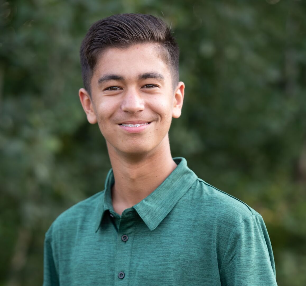 Young man smiling outdoors in a green shirt.