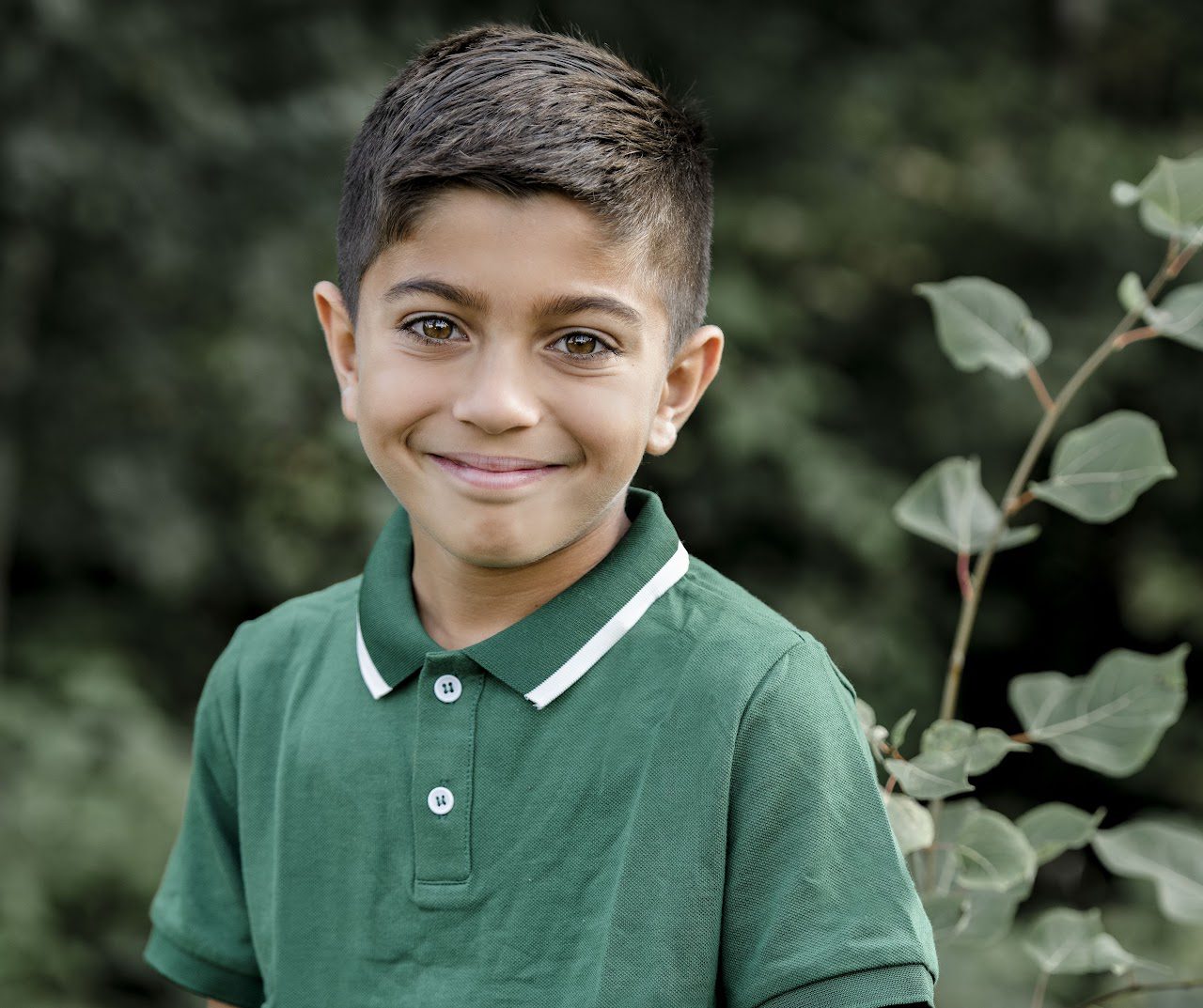 A smiling boy in a green polo shirt outdoors.