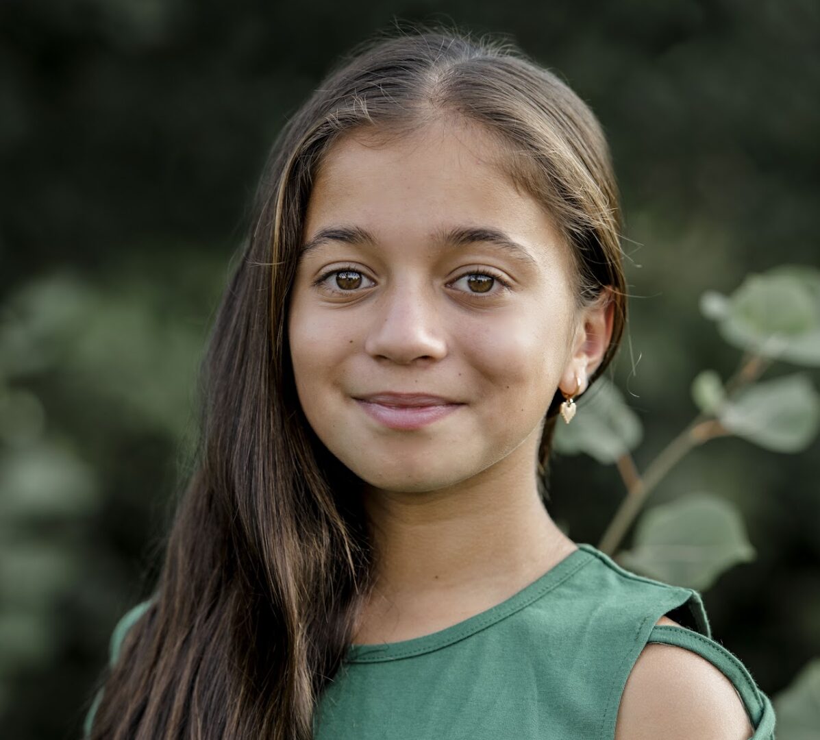 Portrait of a young girl with long hair and a green top, smiling softly.