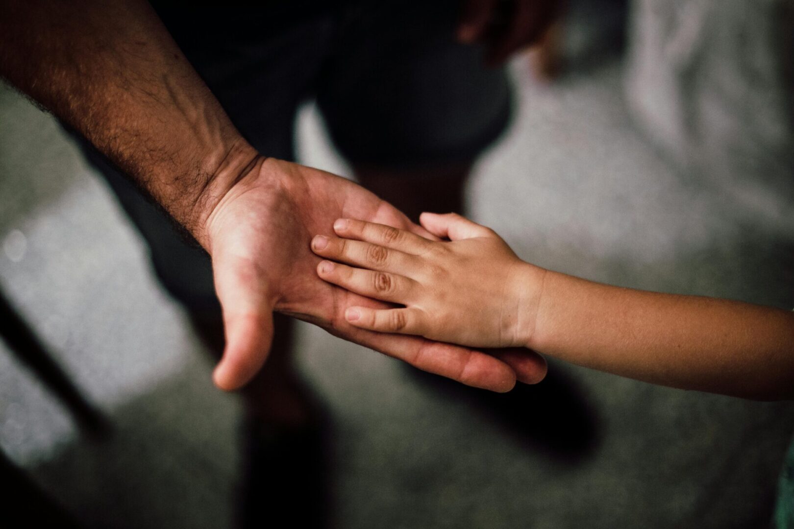 An adult hand gently holding a child's hand symbolizing care and protection.