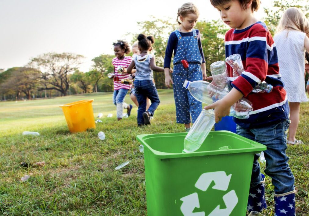 Children recycling plastic bottles outdoors in a park.
