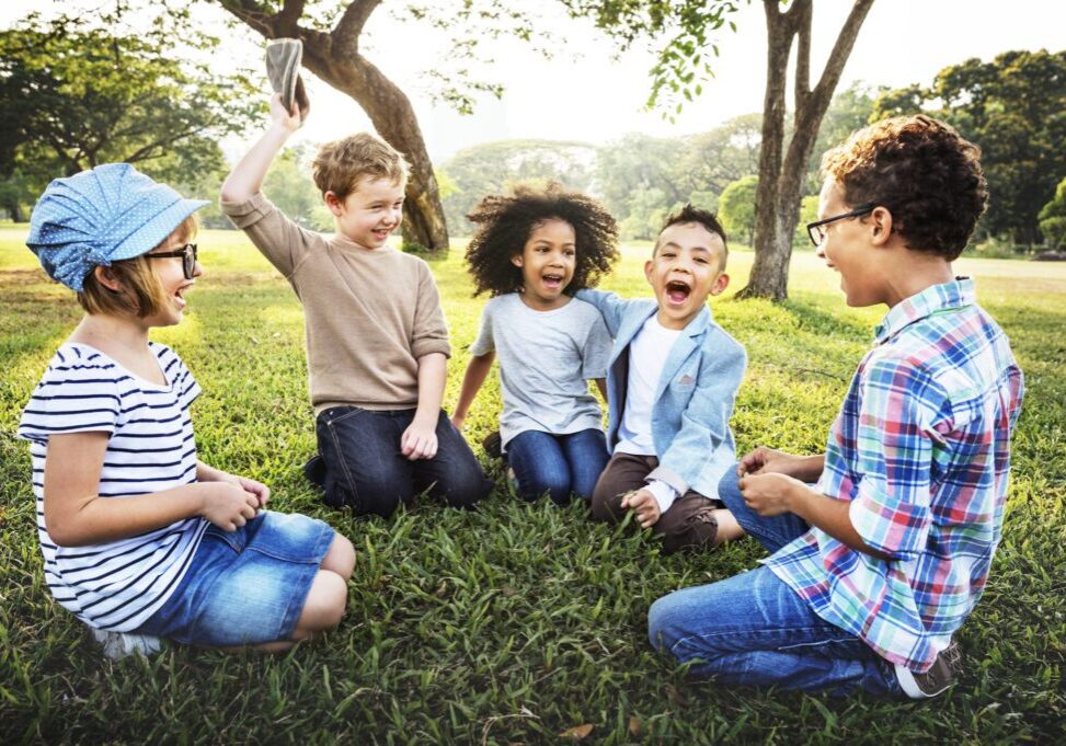 A joyful group of children sitting on grass and laughing together.